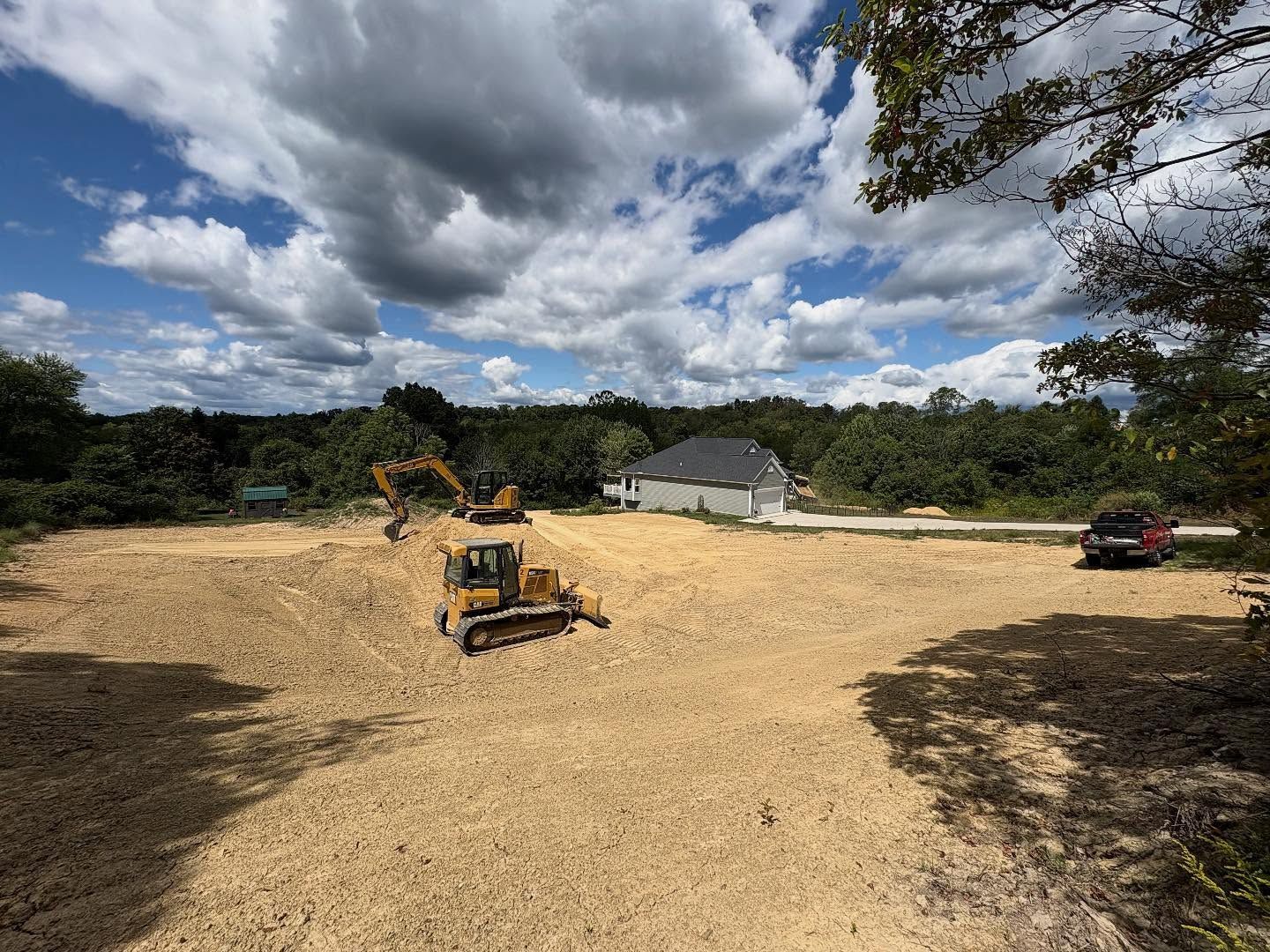 Construction site with two excavators on a cleared dirt lot under a cloudy sky