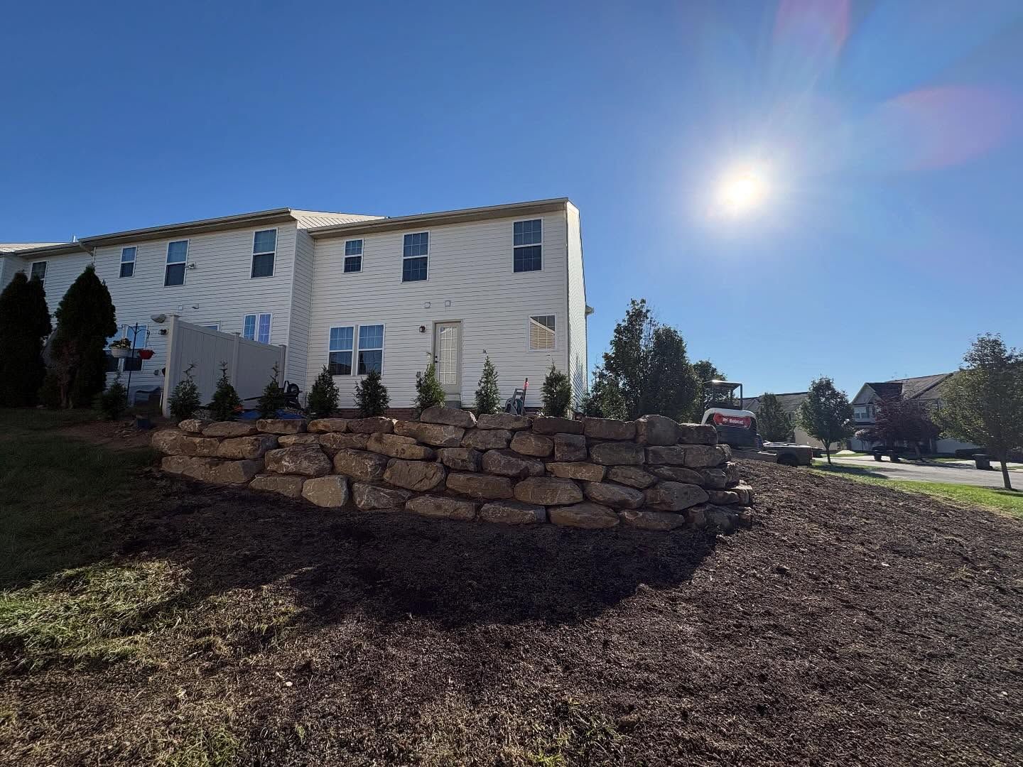 White house with stone retaining wall on a sunny hillside under a bright blue sky