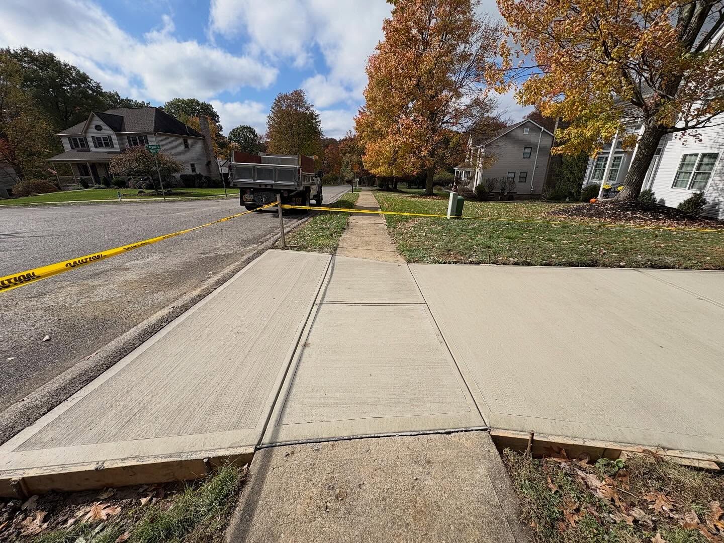 Sidewalk ending at a street crossing with a parked truck and autumn trees in a suburban neighborhood