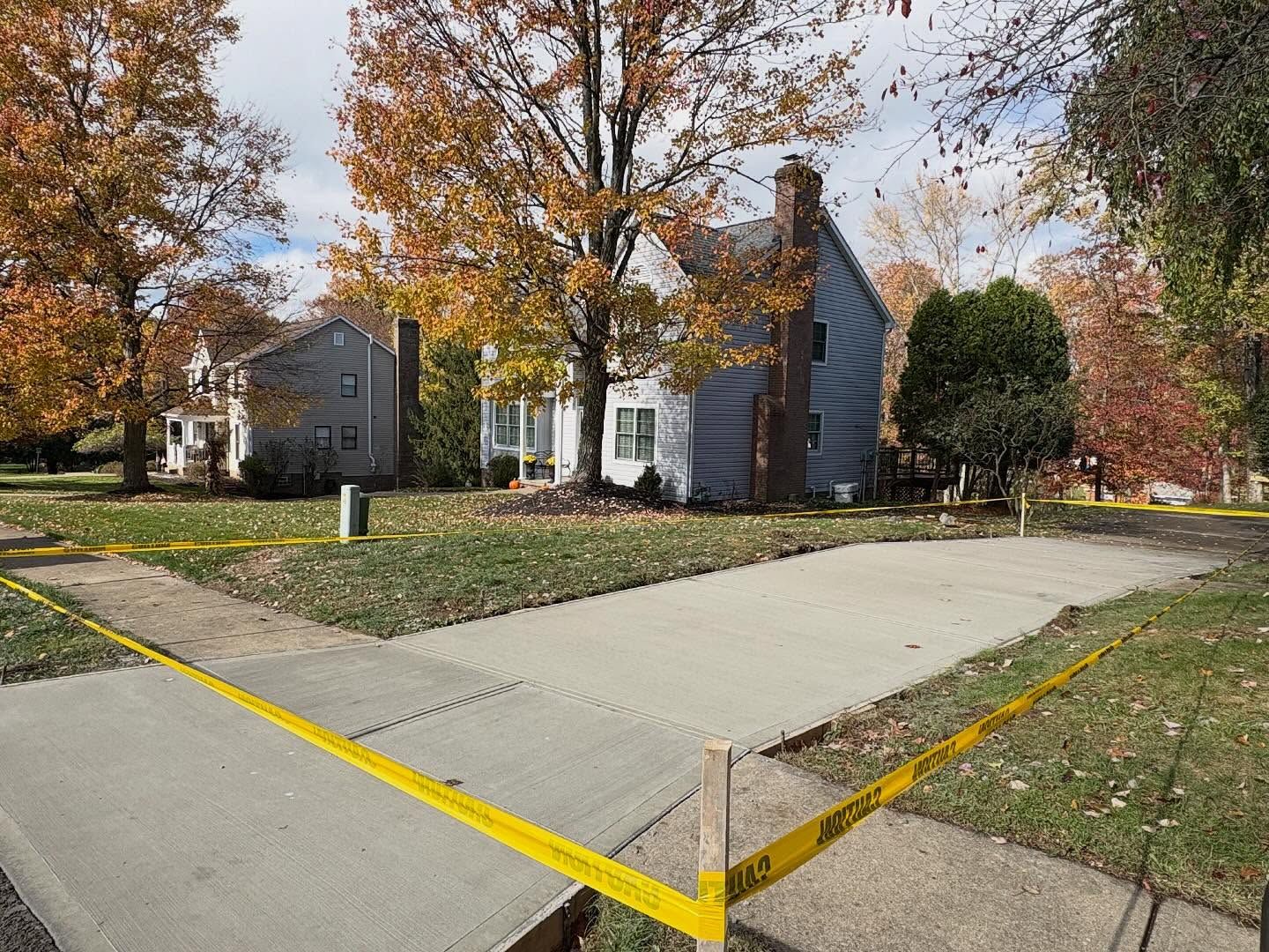 Residential street corner with houses, autumn trees, and a yellow-marked sidewalk ramp