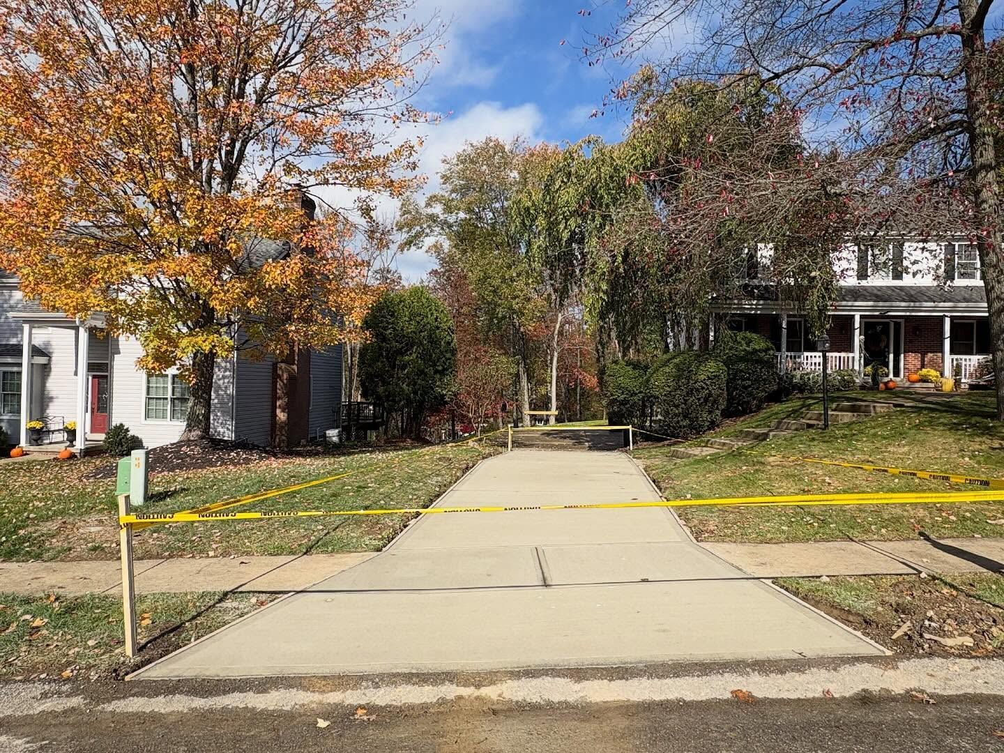 Concrete walkway blocked by yellow caution tape between autumn trees and houses