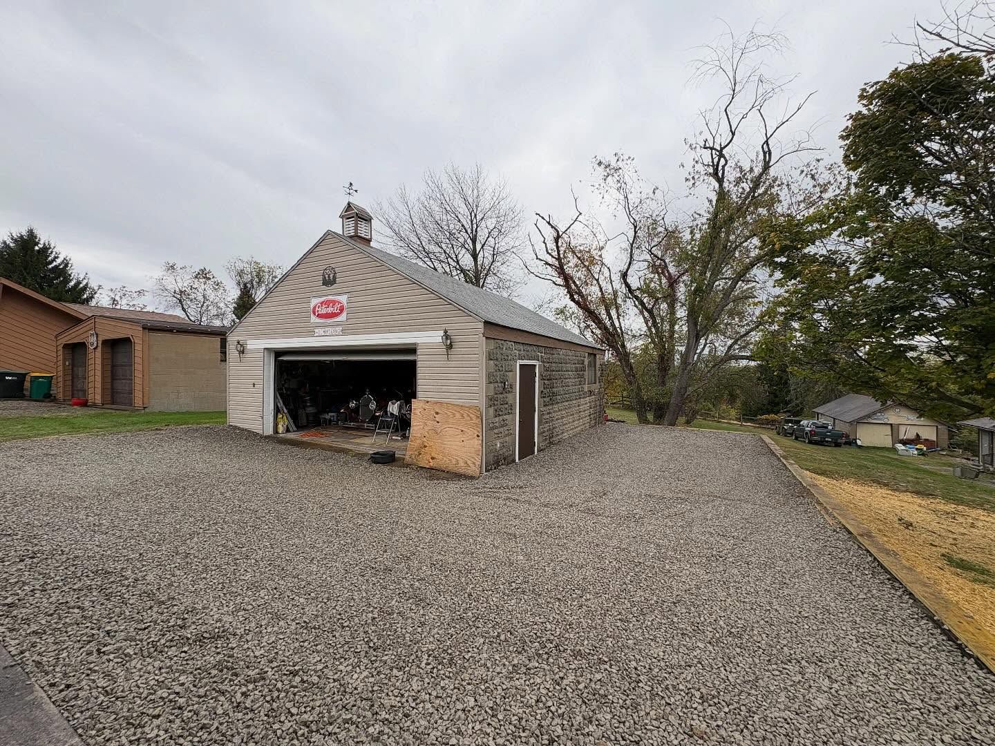 Gravel driveway leading to a small white garage with an open door in a rural yard
