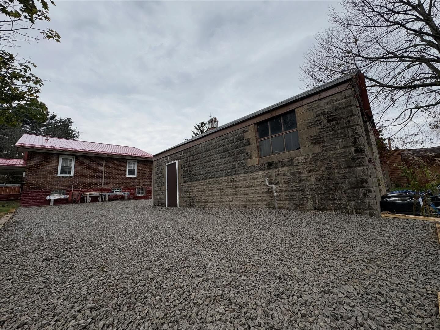 Gravel driveway beside a red brick house and a weathered wooden garage under a cloudy sky