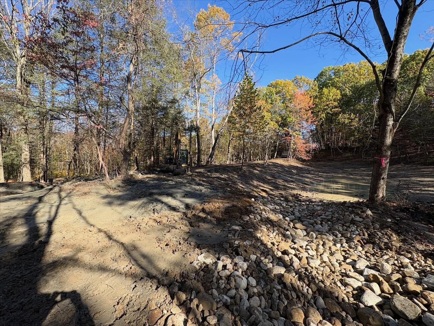 Dirt road beside a rocky streambed in a wooded area with autumn trees and blue sky