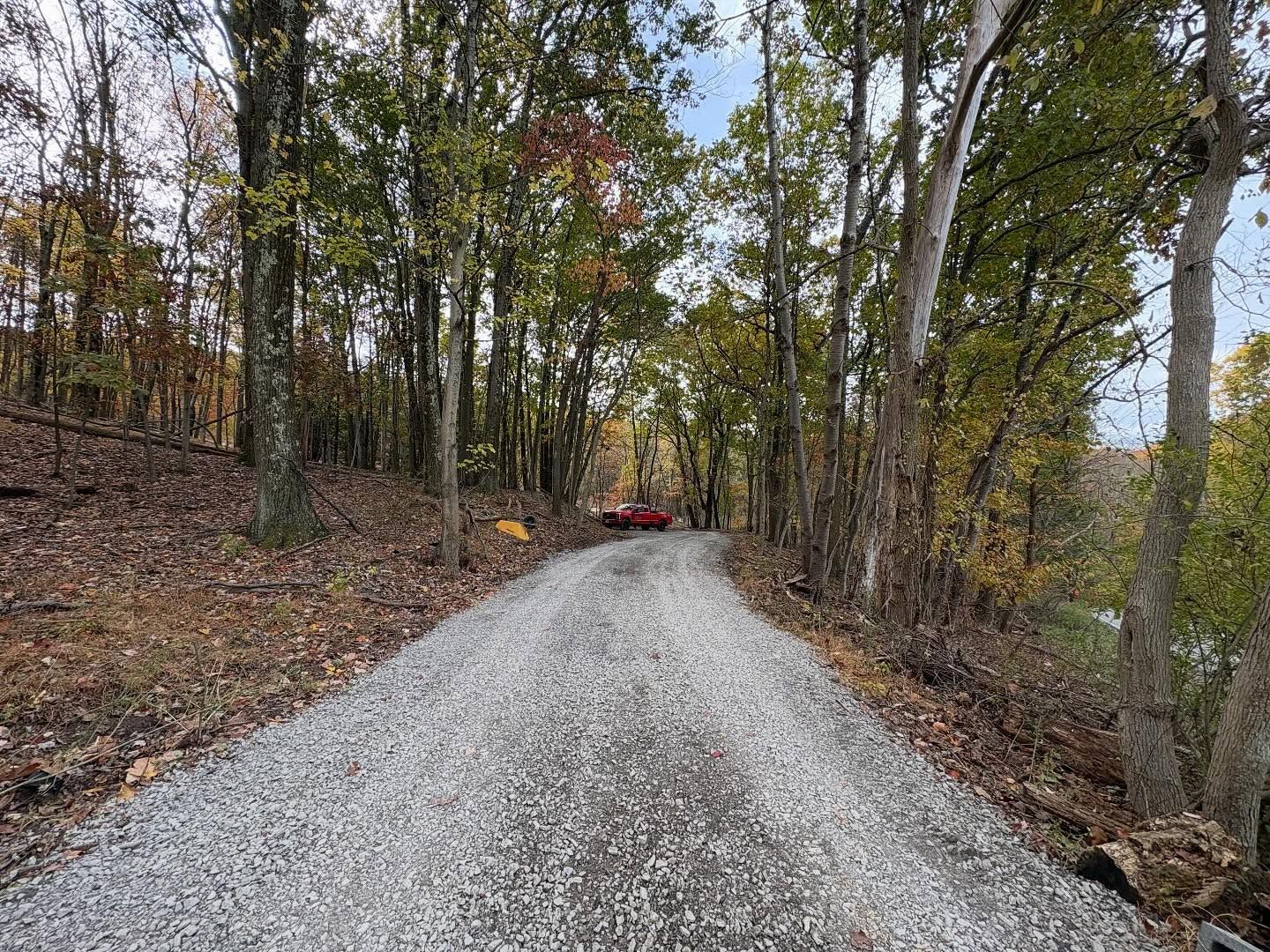 Gravel road through a wooded forest with a red vehicle in the distance