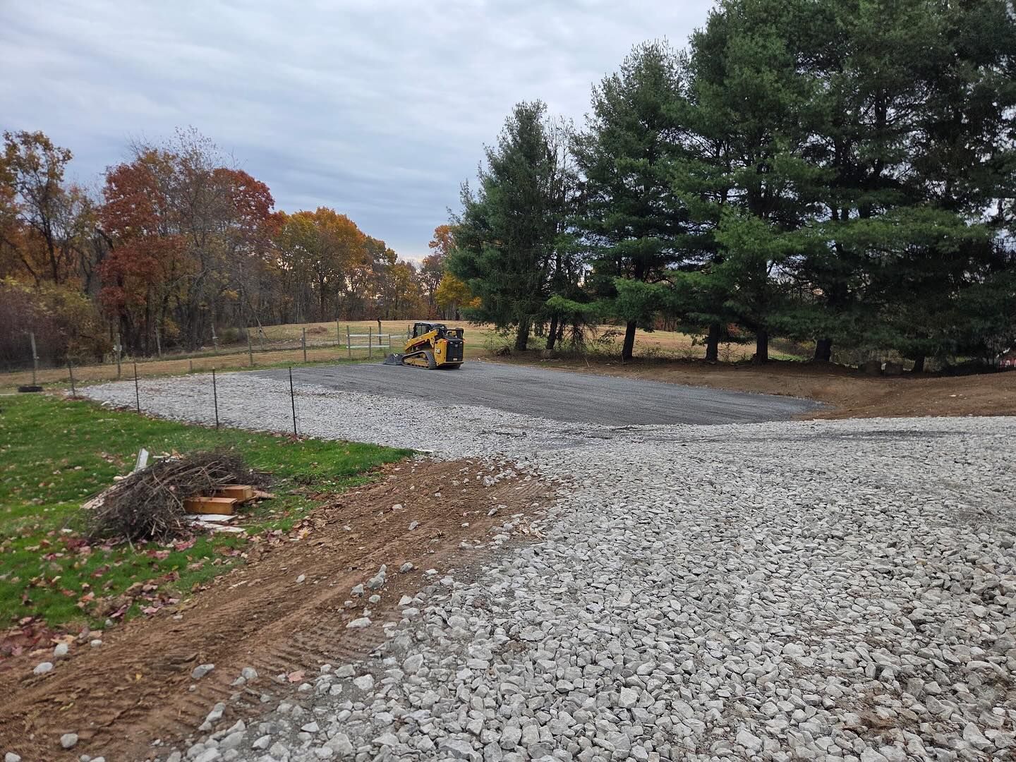 Gravel driveway under construction with a small bulldozer, bordered by trees in autumn.