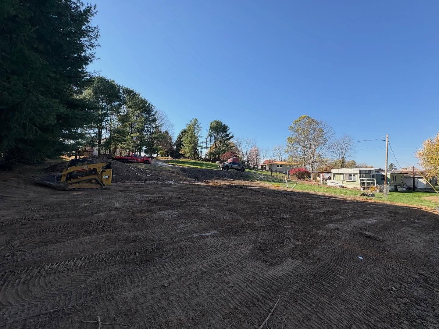 Cleared construction site with bulldozer, dirt slope, and trees under a blue sky