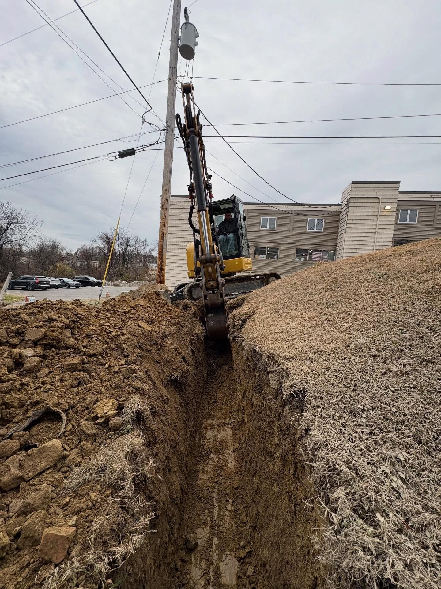 Backhoe digging a deep trench beside a utility pole on a muddy street at a construction site