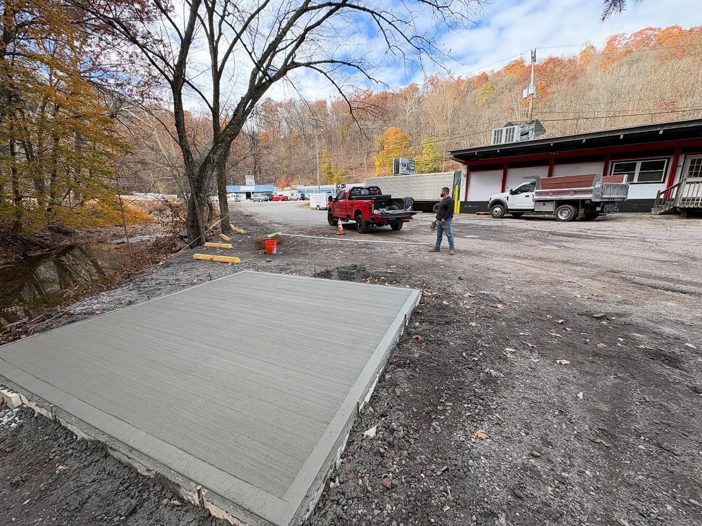 Concrete slab at a construction site with workers, a red truck, and a building in the background.