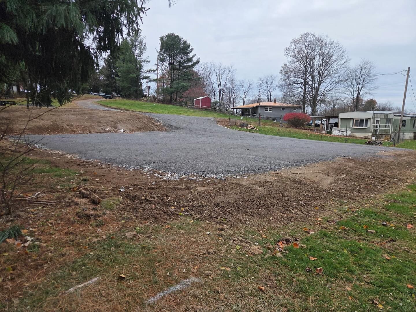 Gravel driveway pad on a grassy lot with trees, a red shed, and mobile homes in the background