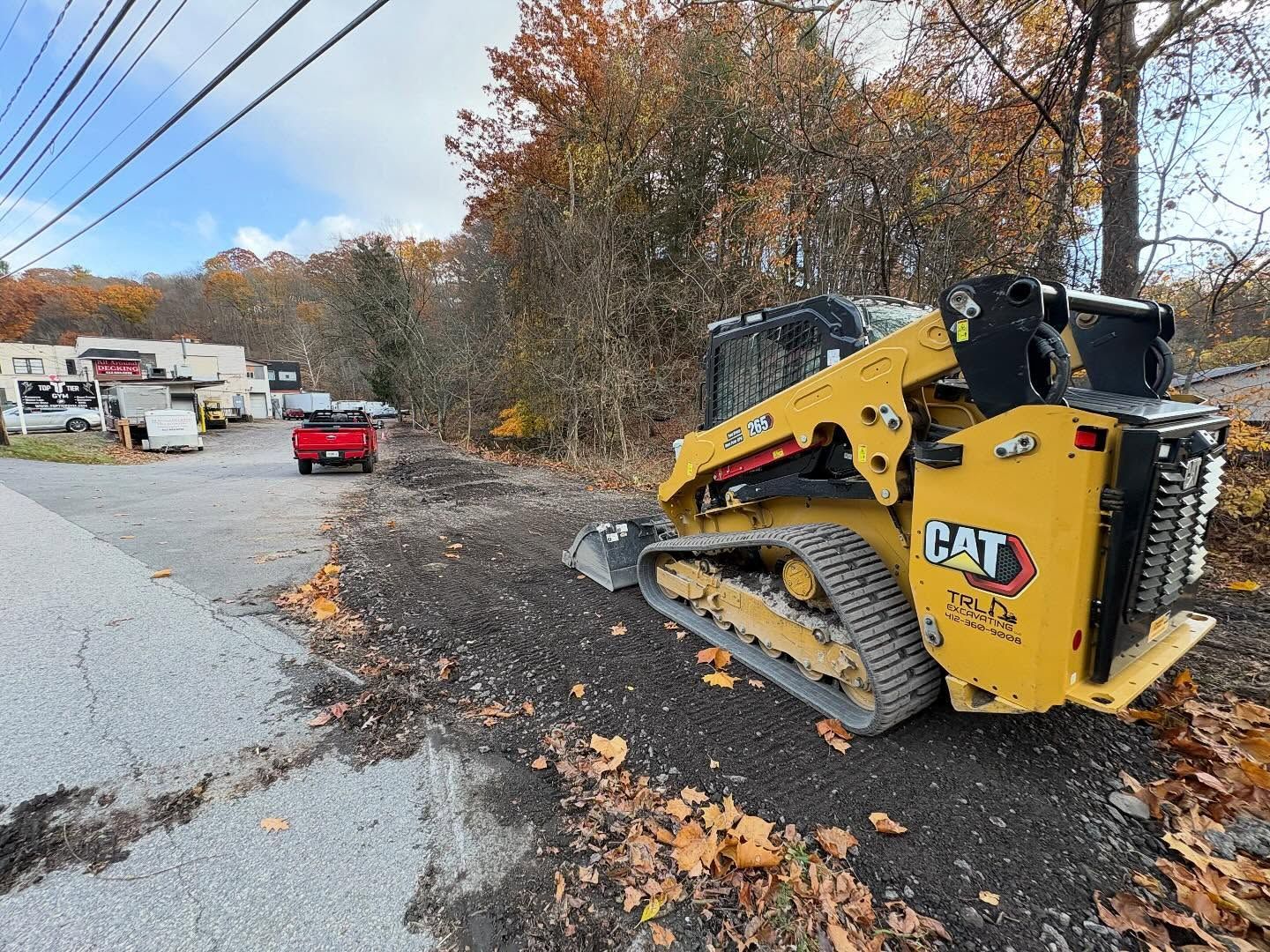 Yellow CAT skid steer scraped on a wet roadside after a crash, with debris and a red truck nearby