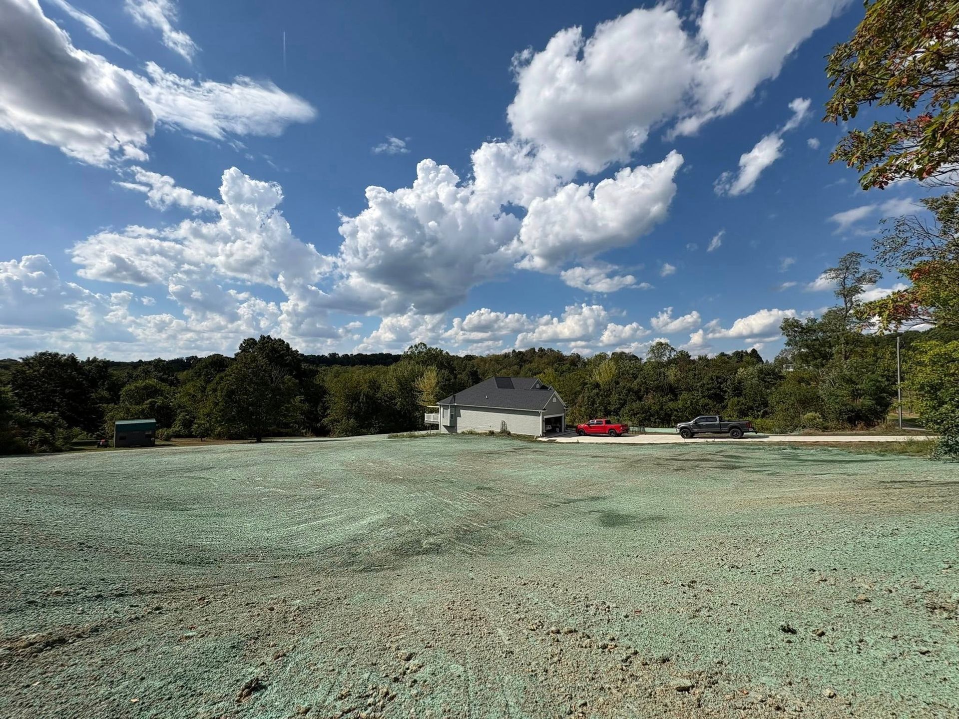Open grassy field with a small white house, red car, and partly cloudy blue sky