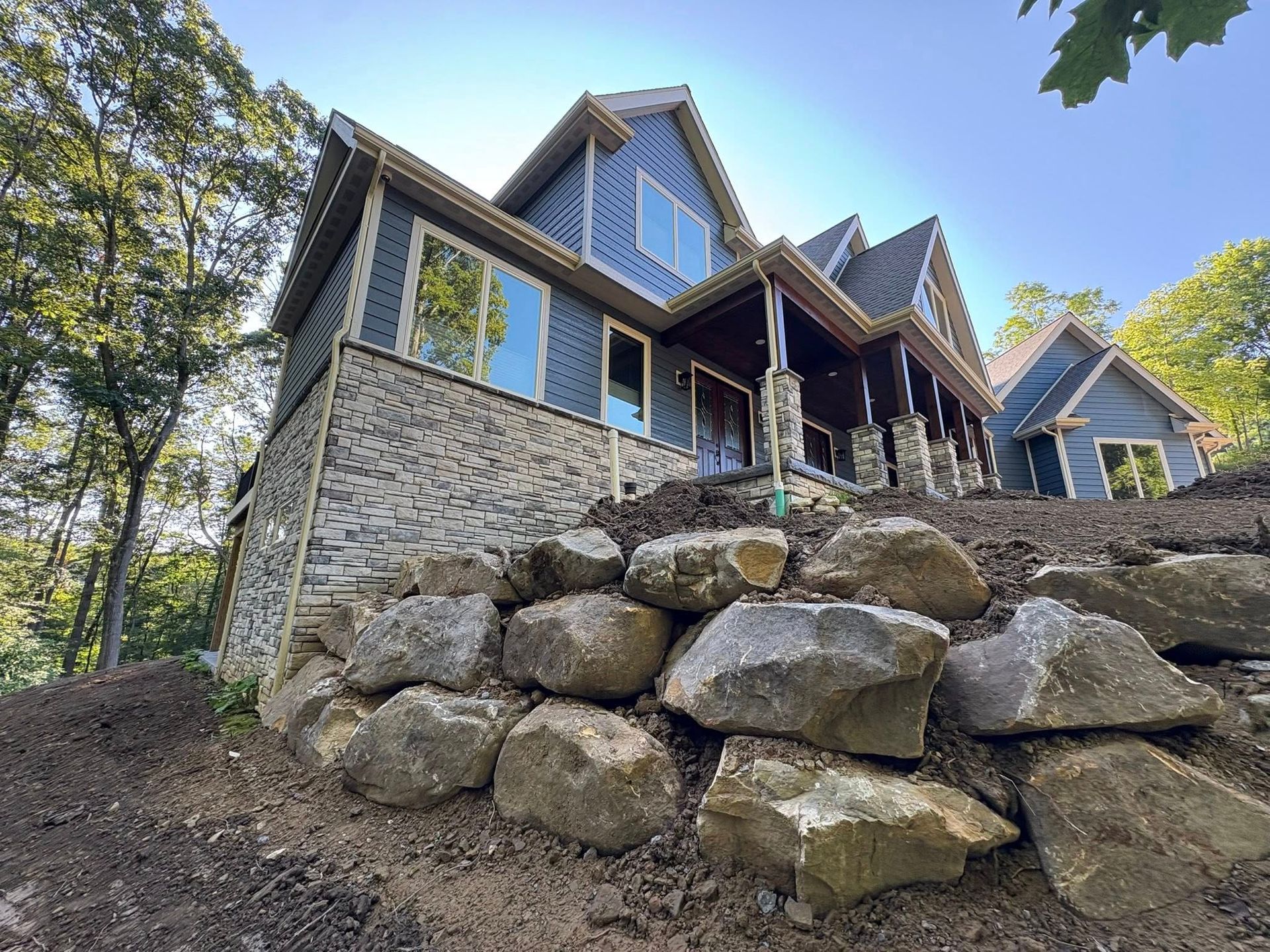 Stone house with blue-trimmed windows on a rocky hillside under trees and a bright sky