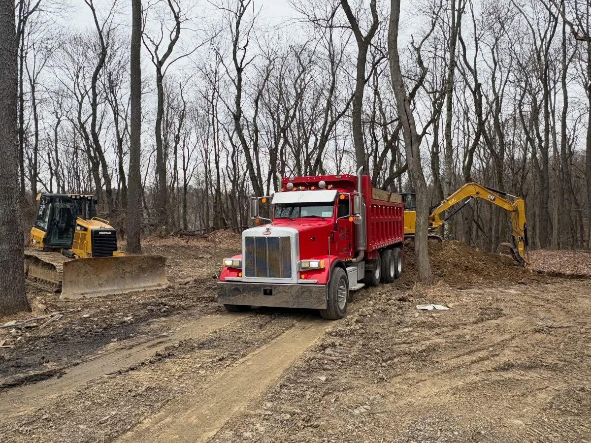 Red dump truck and excavator at a muddy construction site in leafless woods