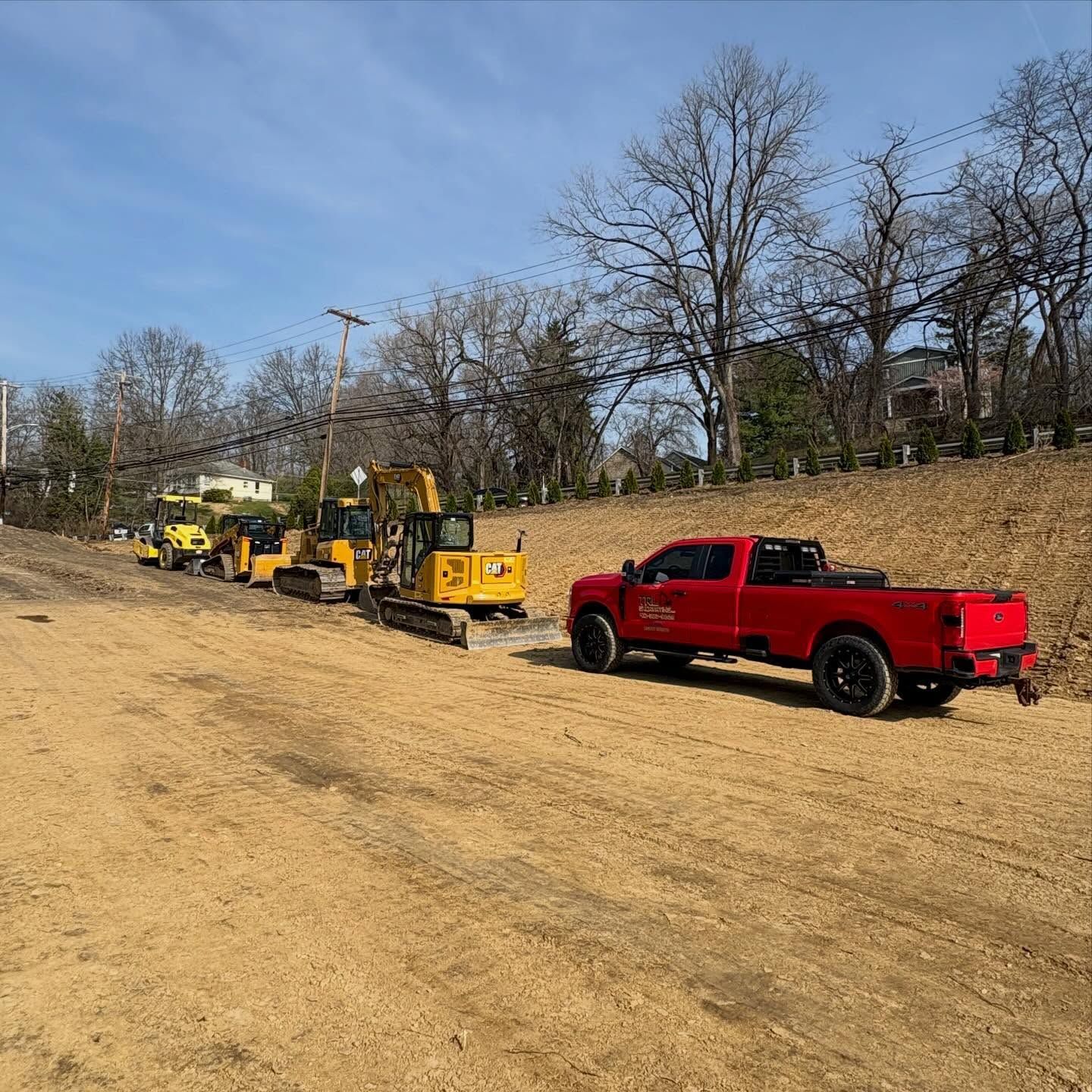 Red pickup truck towing yellow construction equipment on a dirt lot under a clear sky