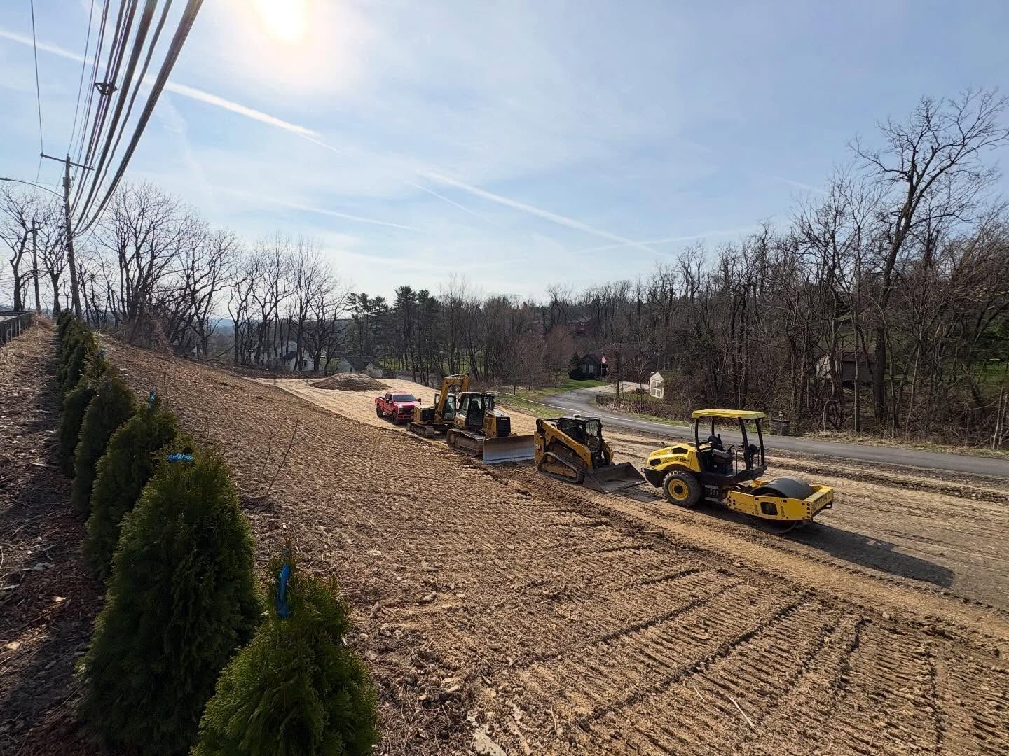 Road construction equipment grading a dirt embankment beside a highway under a clear sky
