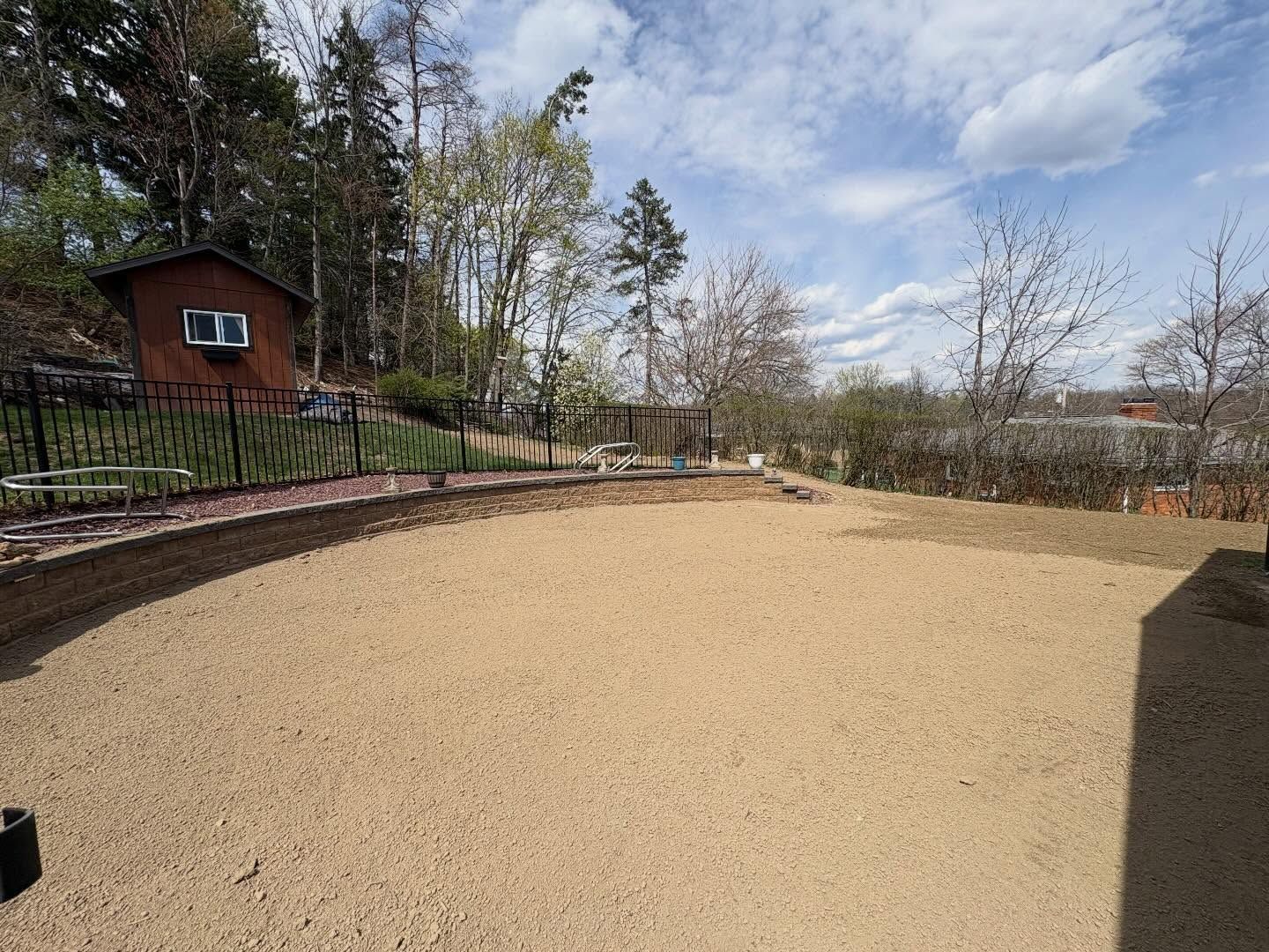 Wide gravel yard beside a small red cabin and trees under a partly cloudy sky