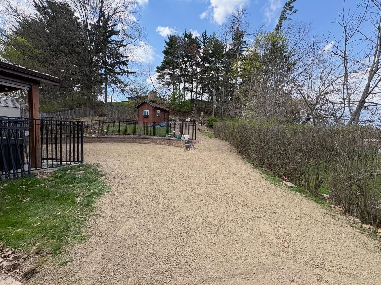 Gravel path leading to a small wooden cabin and trees under a partly cloudy sky