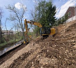 Yellow excavator working on a muddy hillside beside a stream and trees