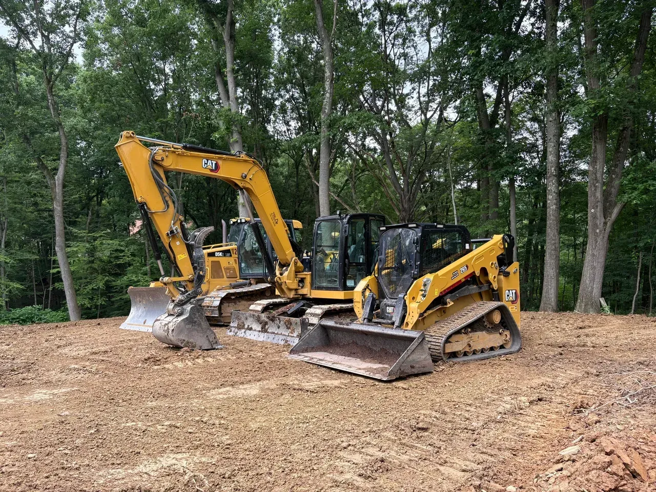 Two yellow construction machines parked on dirt in a wooded clearing