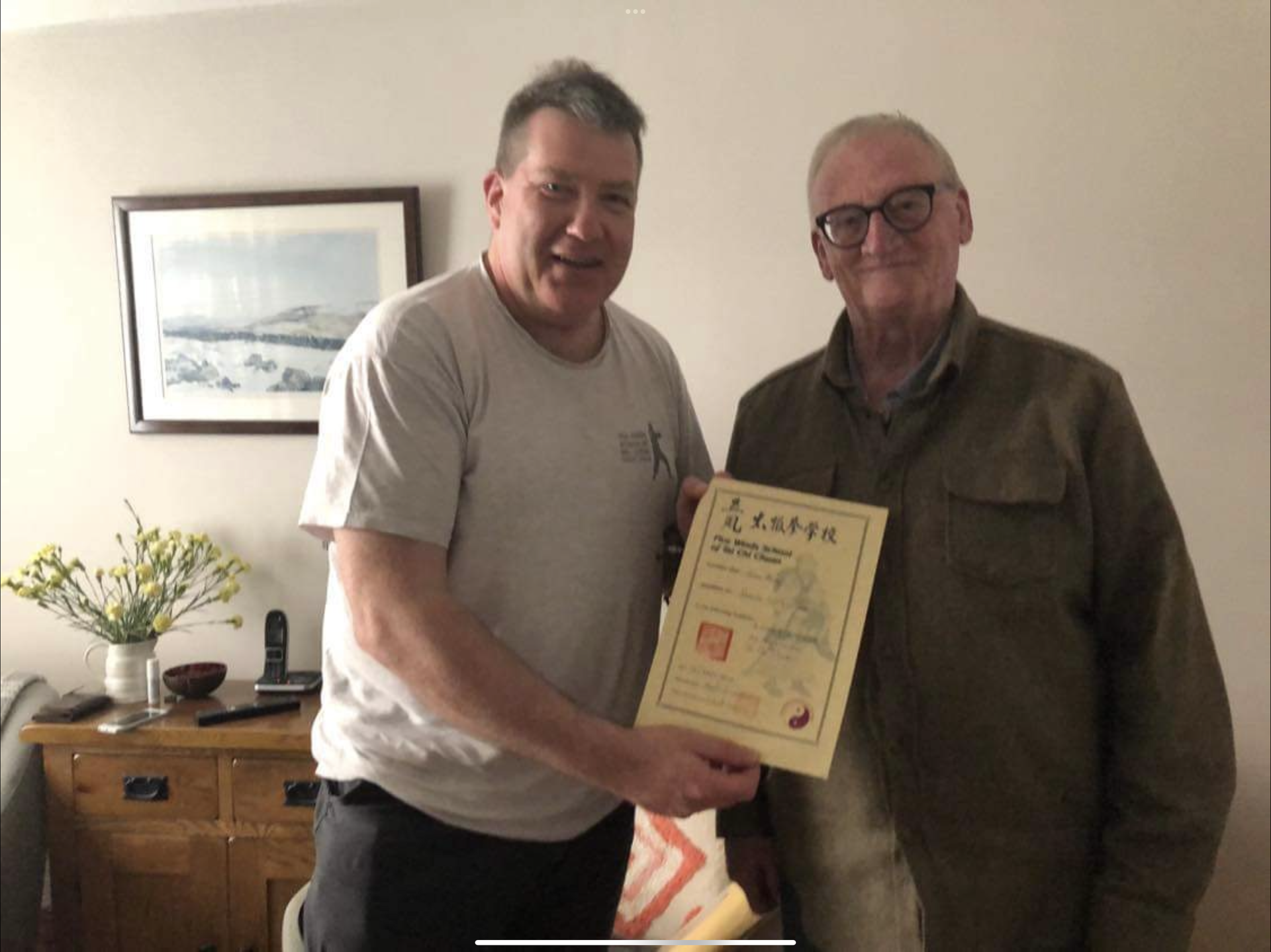 Two men are shaking hands and one is holding a certificate John getting his teaching certificate from Ian Cameron Five Winds Tai Chi Chuan