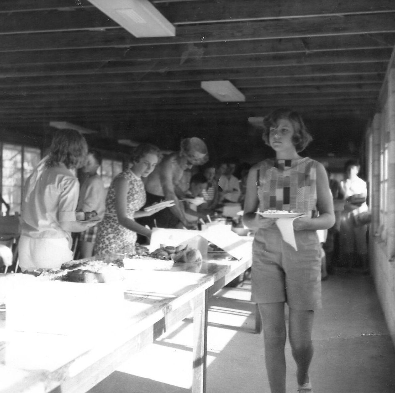 People at a long table inside a building with a simple roof, likely a cafeteria.