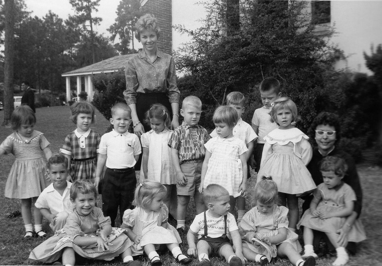 Group of children and two adults posing in front of a building.