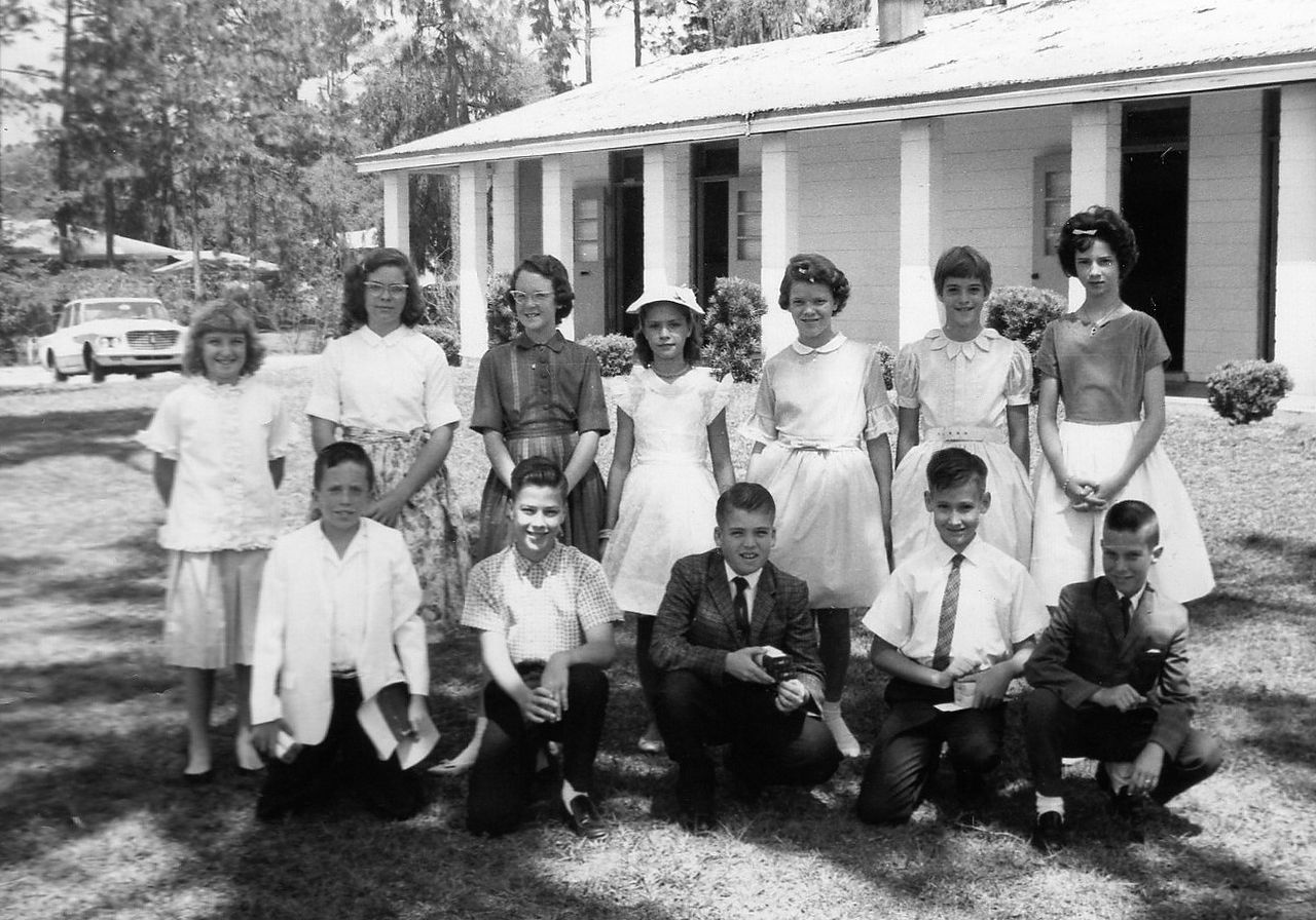 Group of teens posing in front of a white building, some kneeling. Black and white photo.