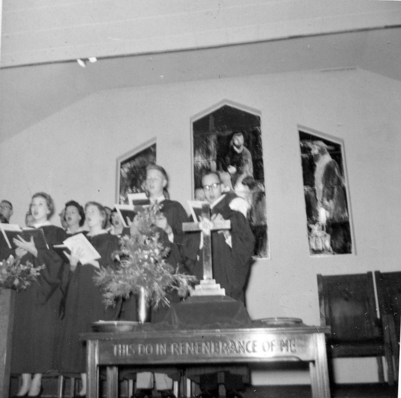 Choir singing in a church with paintings of Jesus. A wooden altar is in front of them.