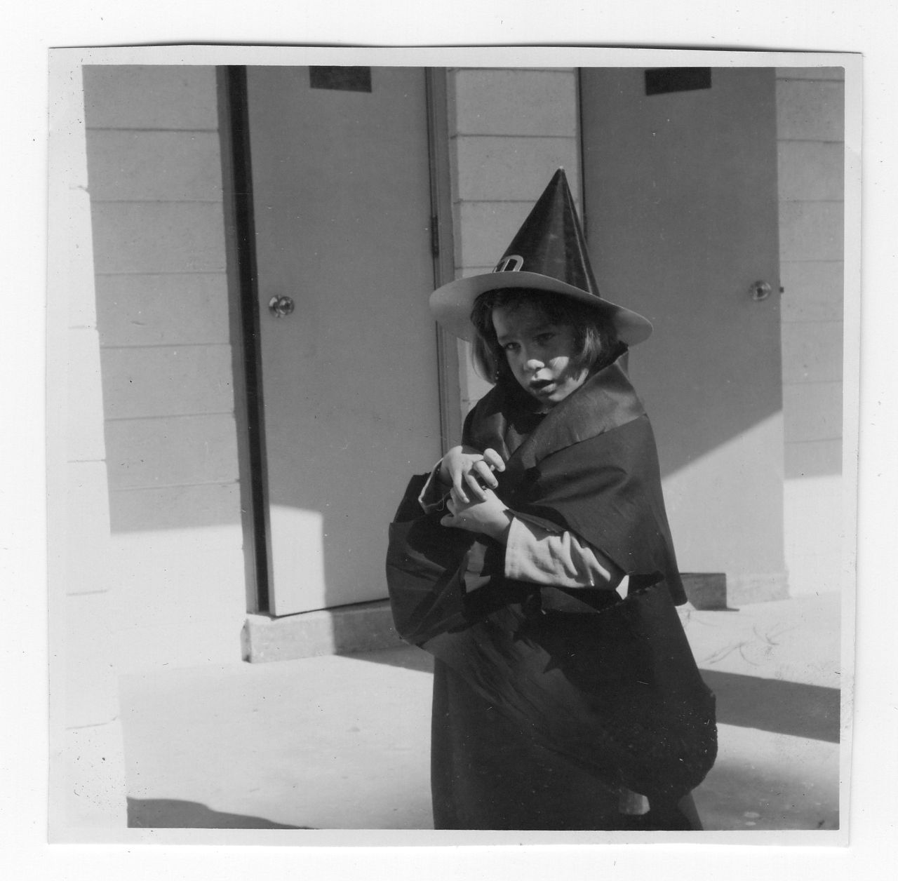 Child in witch costume stands outside, wearing a pointed hat and cloak.