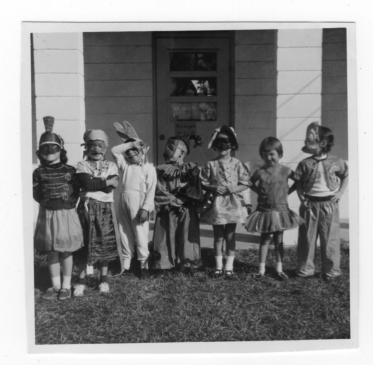 Children in Halloween costumes standing in front of a house with a grass lawn.
