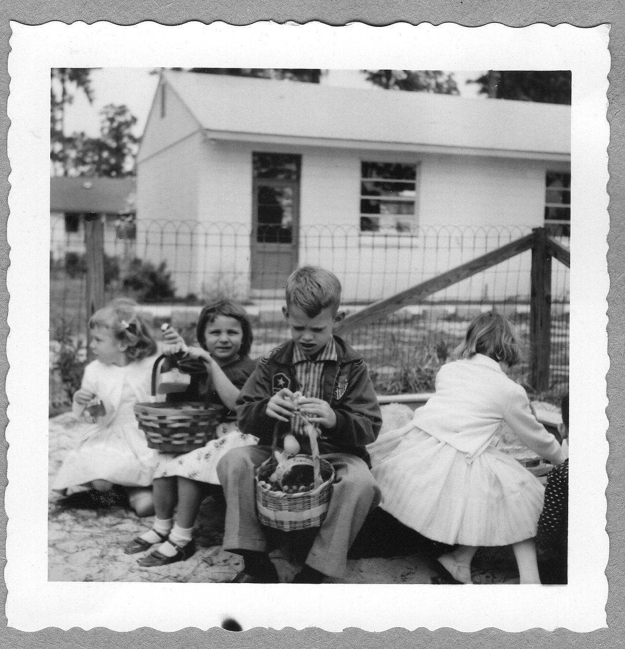 Children with Easter baskets by a small house and fence.