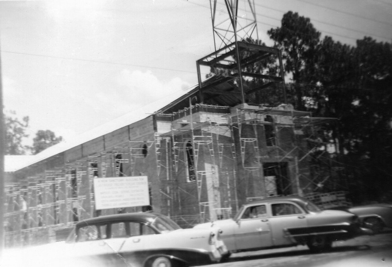 Construction site with cars parked in front. Building under construction, with exposed steel frame.