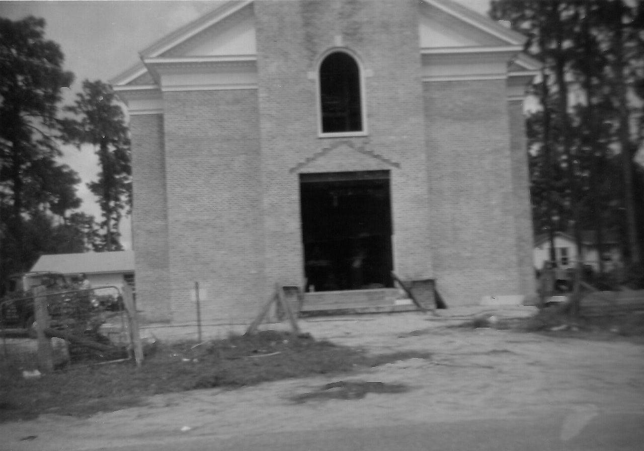 Gray brick church with open doorway, set amongst trees.