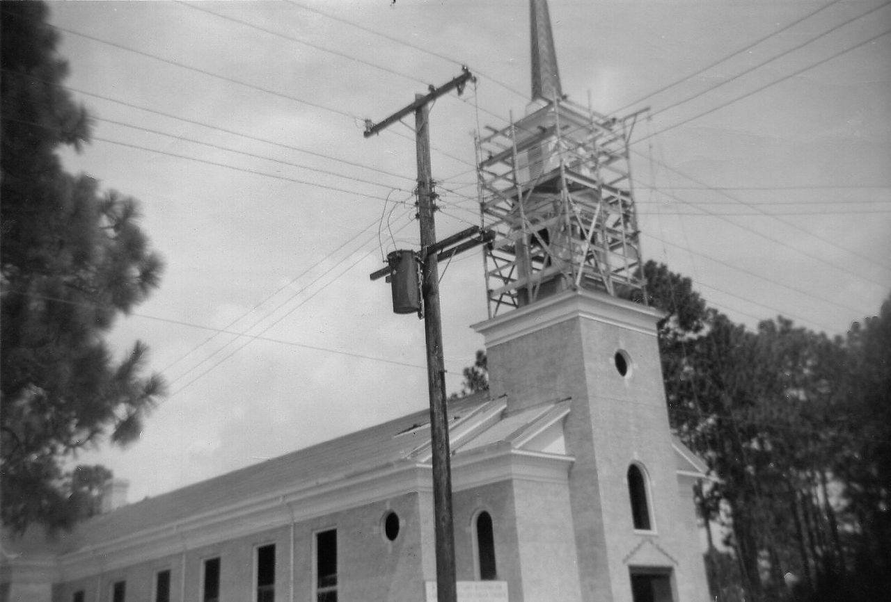 A church with a tower under construction next to a power pole with wires.