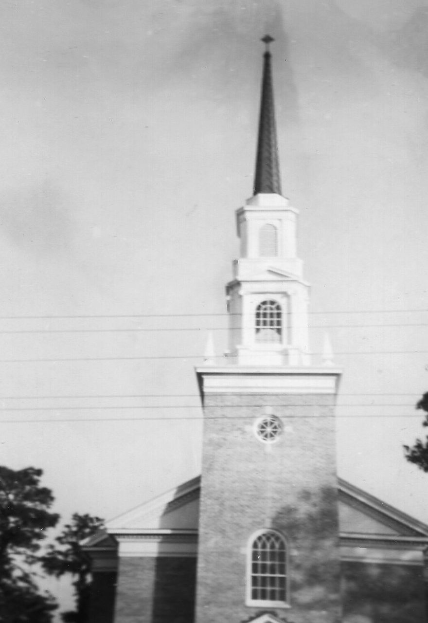 Brick church with steeple, cross on top.