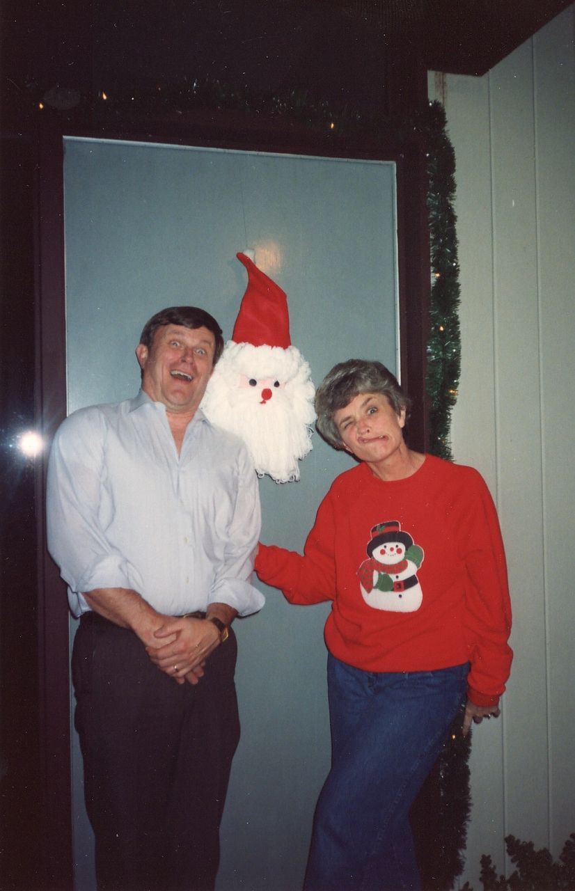 Man and woman pose next to a Santa door decoration. Man laughs, woman points.