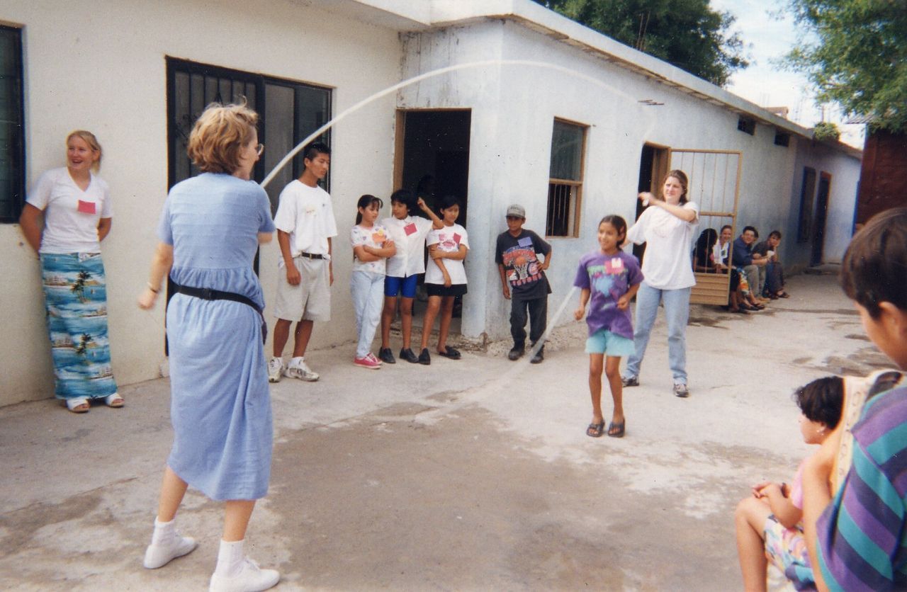 People playing jump rope outside a building; several children watch.