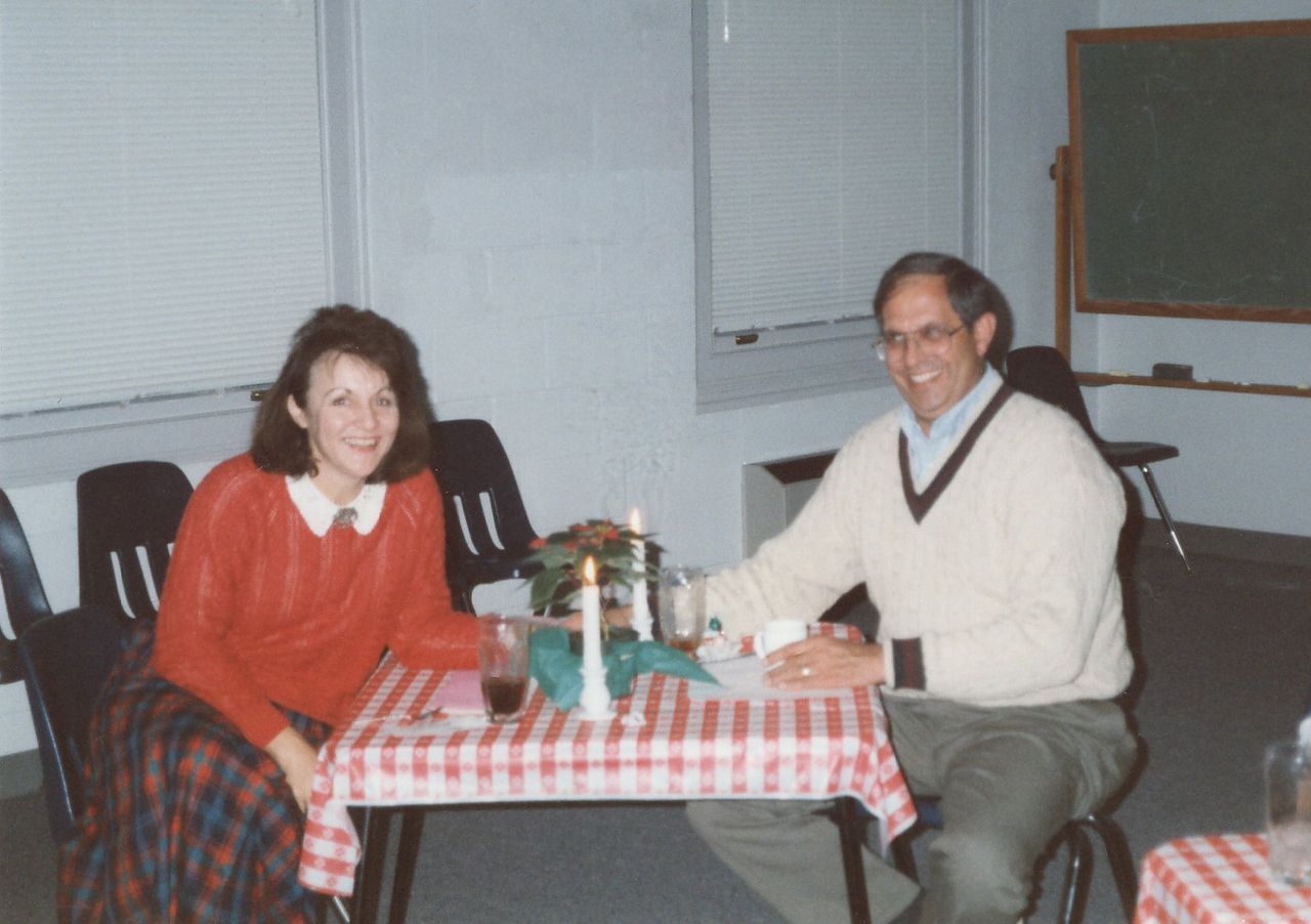 Woman and man at a table set for dinner. They are smiling. Table has a red and white checkered tablecloth.