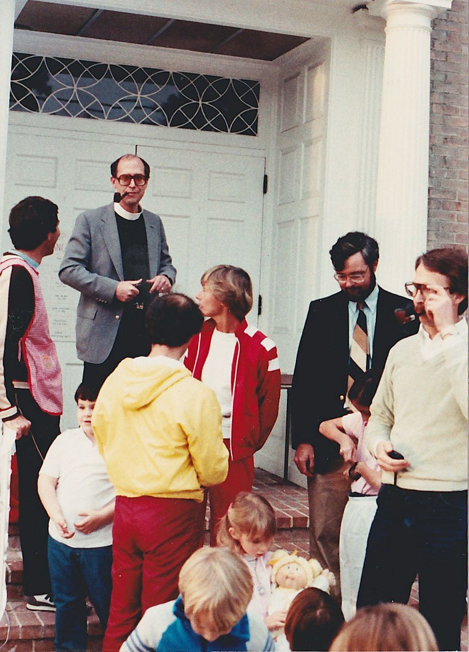 People standing on steps in front of a white building with columns; some are children.