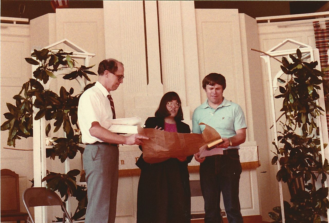 Three people holding a large wooden object indoors, possibly a church.