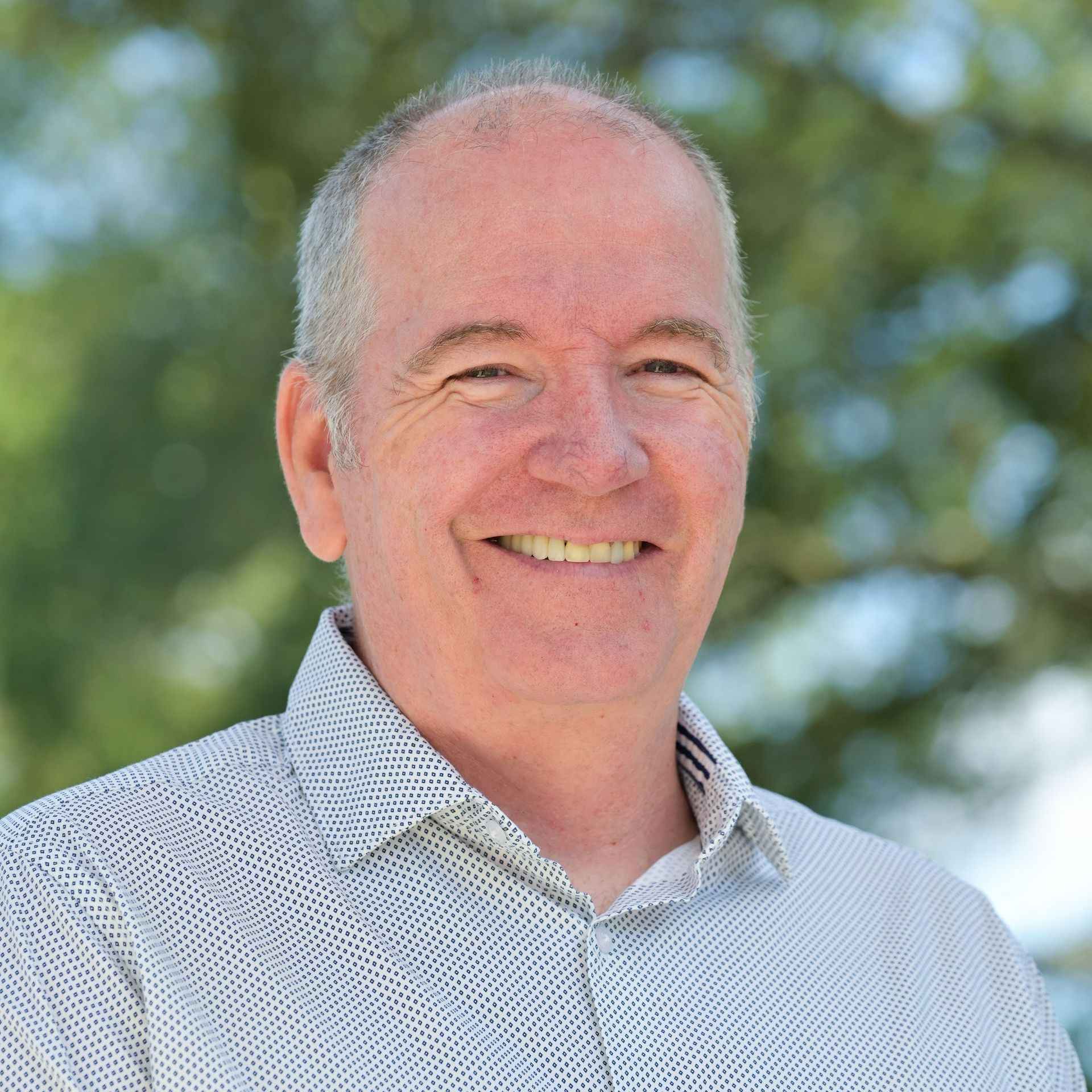 Smiling man in patterned shirt, outside.