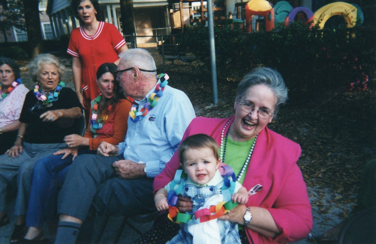 Group of people outdoors, some with leis, smiling. A baby is held by a woman.