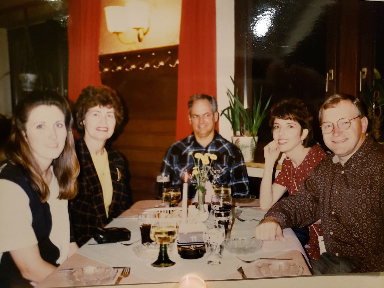 Five people seated at a table in a restaurant; candles and glasses are present.