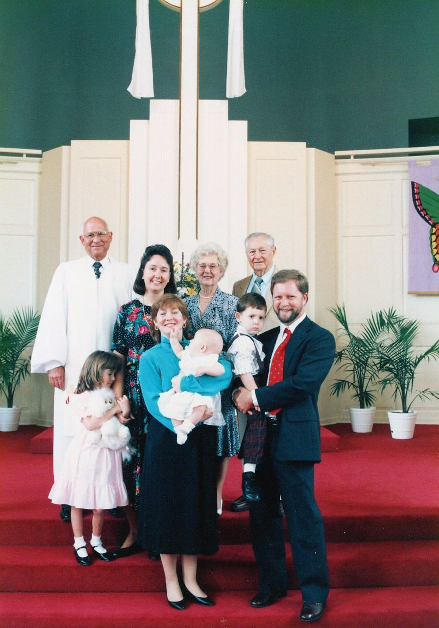 Family stands in front of a church altar. Several people hold children, smiling.