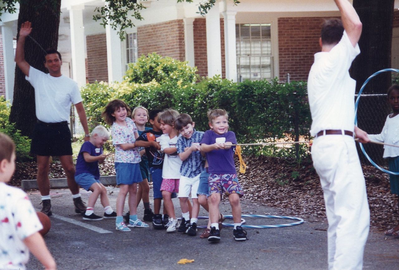 Children and adults playing with hoops outdoors, holding hands, and stretching arms.