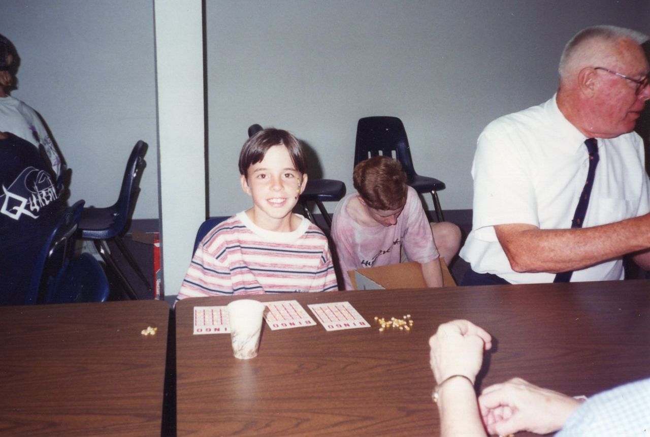 Boy smiling at a table, playing a game with cards and a man looking on.