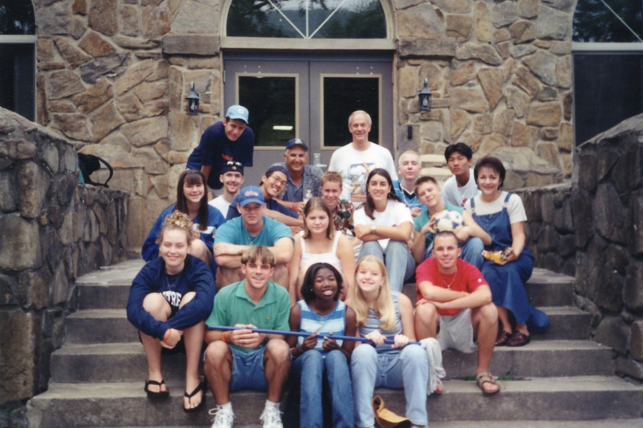 Group of people on stone steps in front of a stone building. People smiling, some holding objects.