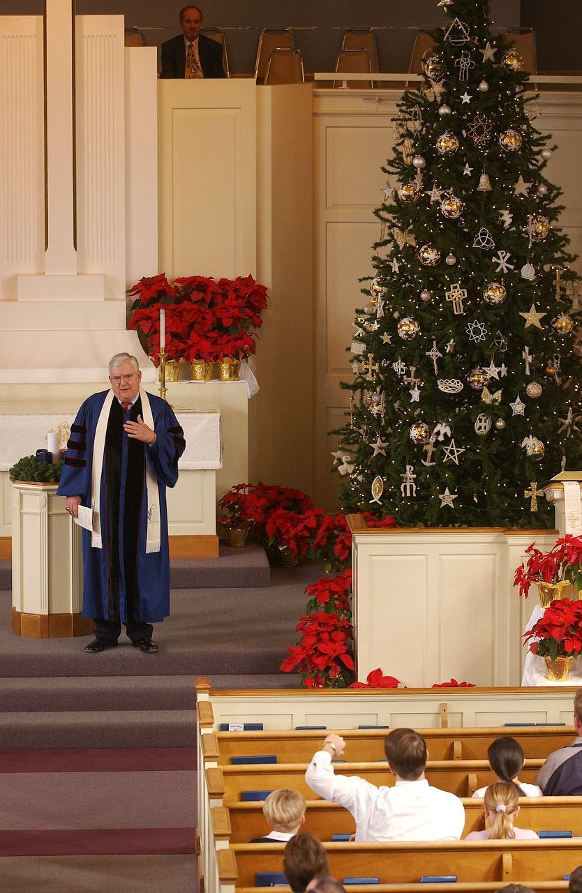 Man in robe speaks from podium in church decorated for Christmas.
