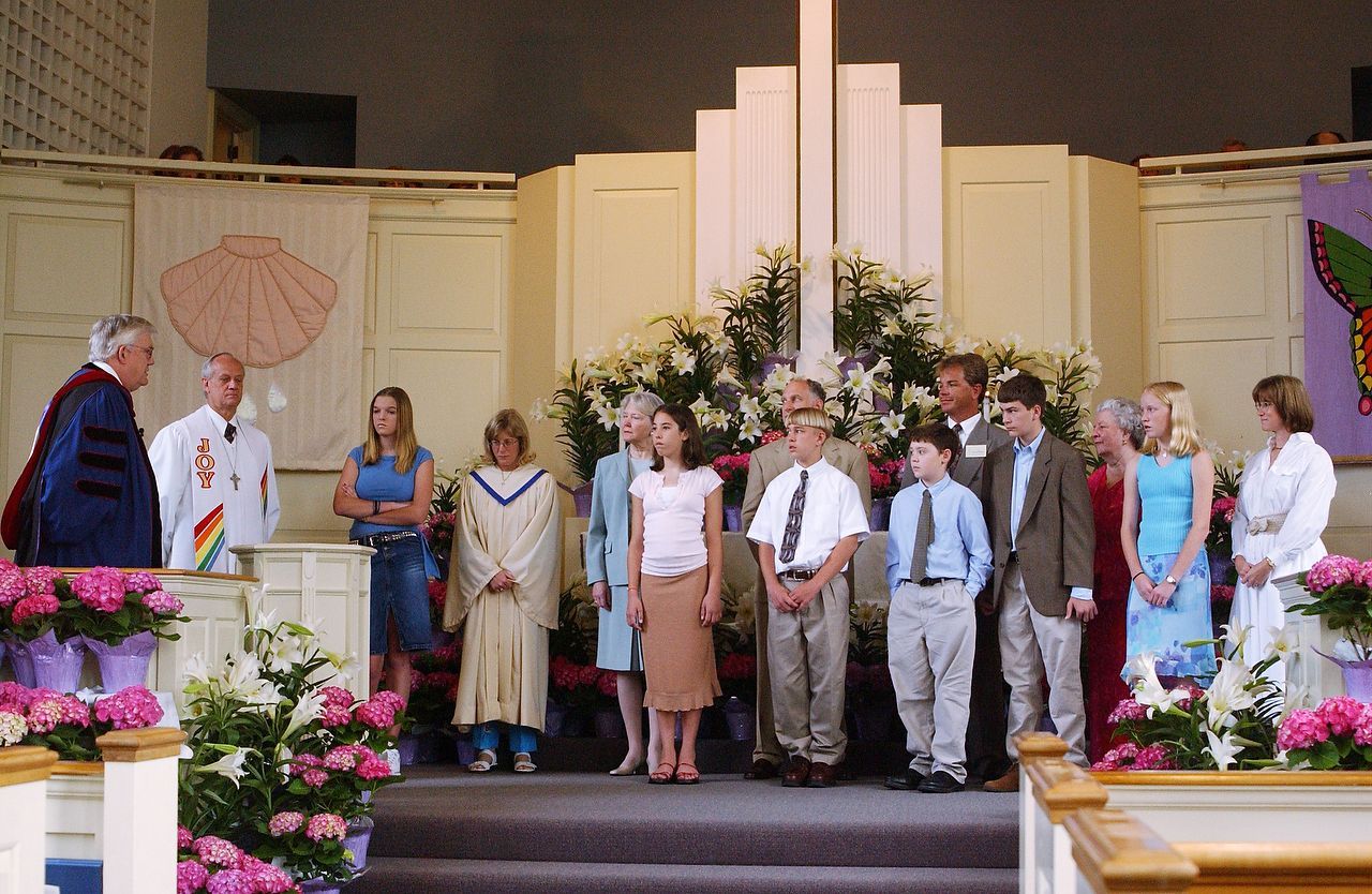 Group of people at a church altar with flowers. A cross is centered.